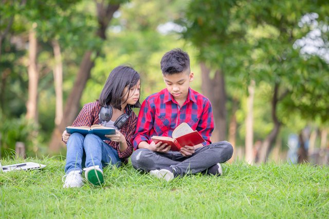 Brother and sister sitting on the grass and reading the book in عربيّةكوم Arrabiacom