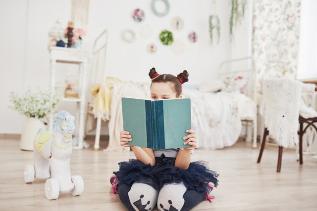 Cute little child girl reading a book in the bedroom Kid with crown sitting on the bed near window عربيّةكوم Arrabiacom