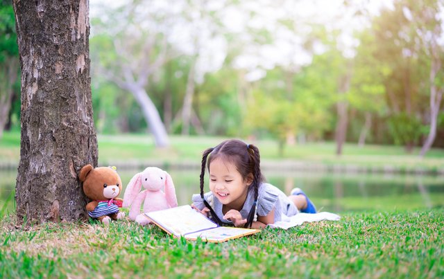 cute little girl reading a book while lying with a doll in the عربيّةكوم Arrabiacom